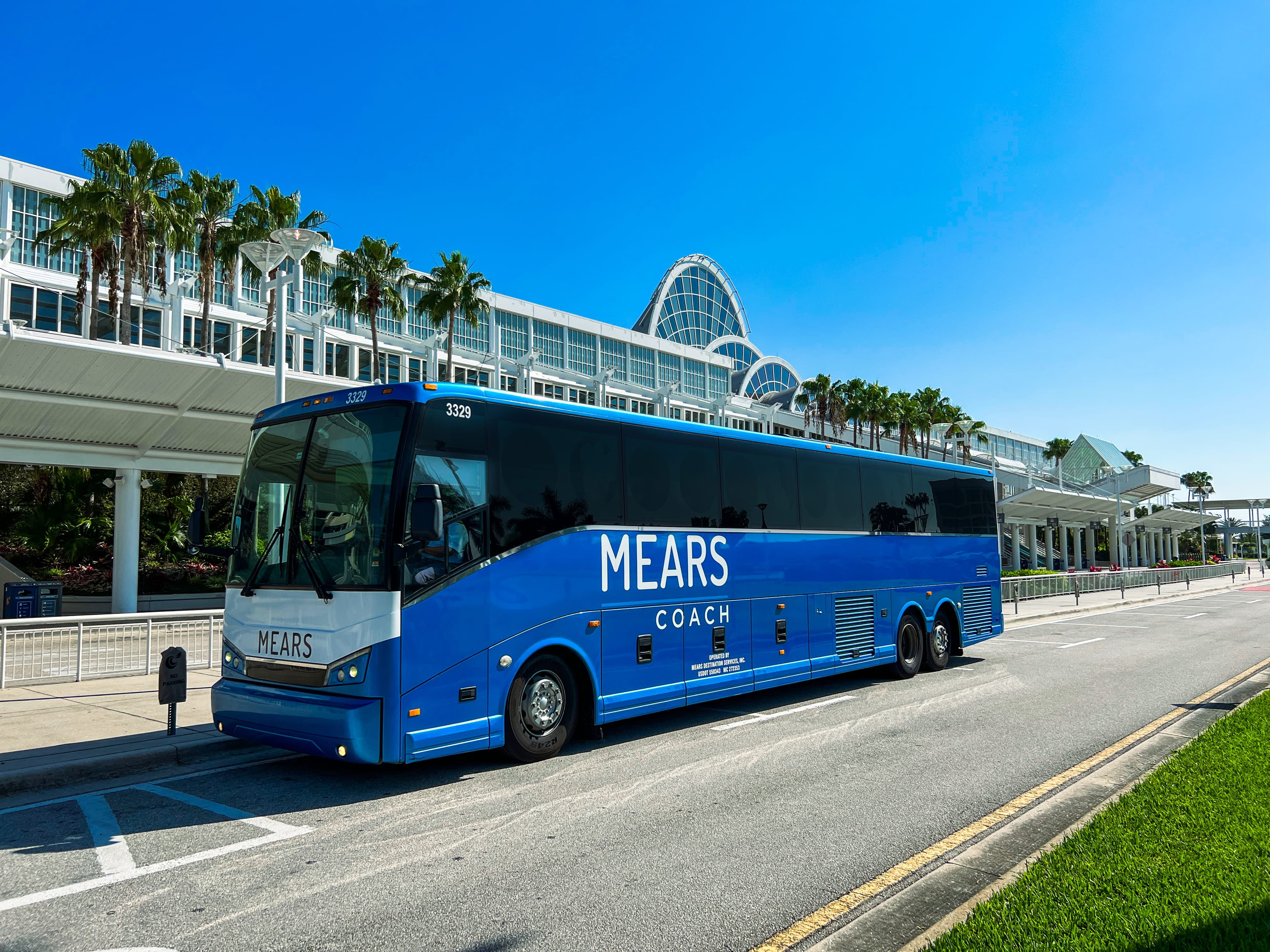 Smiling Motorcoach Operator stands beside a yellow and white Mears coach bus.